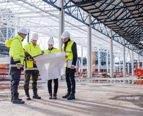Group Of Engineers With Blueprints Standing On Construction Site